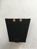 Two small yellow stone stud earrings displayed on a black earring stand.