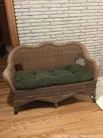 Front view of the rattan loveseat showing the green tufted cushion and woven backrest design.