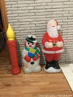 Wide shot of all three blow mold figures (candle, snowman, Santa) against a brick wall