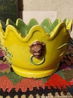 Close-up view of side of yellow porcelain bowl showing lion head handle with ring.