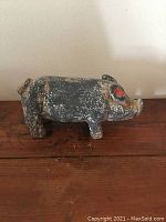 Side angle of vintage ceramic pig ornament showing black paint with wear and chips, red accents on ear and snout, placed on wooden surface.