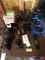 Overview of lot on wooden surface showing walkie-talkies, lens boxes, remote, cable, antenna, line chooser, Audio Solutions device