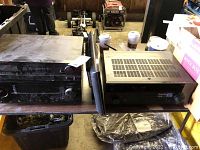 Yamaha receiver and two other electronic units on a table with dust and storage items around.