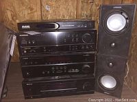 Stack of four audio components: Audio Authority CD player on top, Pioneer VSX-311 receiver, Yamaha RX-397 receiver, and Sherwood receiver at bottom. All have black finish with controls on front. Components stacked on plywood surface against plywood backdrop.