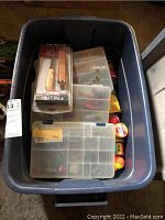 Top view of blue plastic tote container holding three plastic compartment tackle boxes and visible fishing bobbers inside.