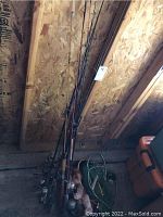 Full view of multiple fishing rods leaning against wood panel wall, some with reels and nets on the floor.