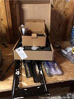 Box and loose metal door hardware on a wooden surface including sliding mechanisms and small packaged items.