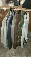 Several men's outerwear jackets in different colors hanging on hangers on a wooden rack. Visible colors include beige, gray, black, brown, camouflage, and white.