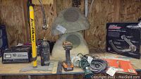 Photo of various items on a wooden shelf including Ridgid drill with battery, spirit levels, bicycle pump, electrical cords, decorative stone pieces, and boxed hardware items