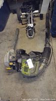 Photo showing both the backpack blower and handheld blower lying on the ground, highlighting the harness and flexible tubing.