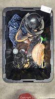 Top view of black bin containing assorted baseball equipment including gloves, helmet, ball and shoe.