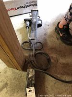 Metal trailer hitch extension showing length and attached wiring cable coiled on top, with floor and shoe for scale.