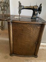 Side view of the wooden cabinet base housing the sewing machine showing curved wood panels and detailed wood grain.