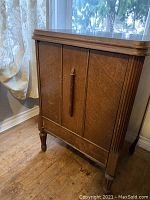 Wooden cabinet housing the sewing machine with paneled doors and wood grain finish.