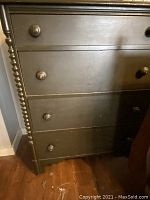 Close-up photo of the lower half of a dark wood dresser showing four drawers with round wooden knobs and decorative spindle details on the side. The wood has visible signs of wear and scratches.