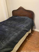 Front view of bed with upholstered wooden headboard covered by black blanket
