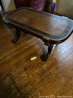 Full view of the coffee table showing wooden top with black border on a wooden floor.