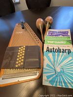 Full view of autoharp showing wooden body, chord bars with buttons, a tuning bar on top, a pair of wooden maracas, and three colorful autoharp music books.