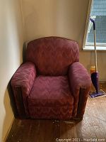 Front view of one vintage armchair showing the red patterned upholstery and wide armrests.