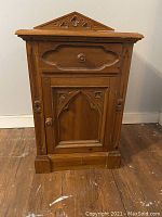 Front view of carved wooden Mexican styled bedside table showing drawer, cabinet door, and triangular pediment carved with quatrefoil design.