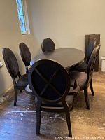 Photo of six black dining chairs around an oval dining table in a room with wood flooring and a stained glass window.