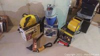 Karcher pressure washer box, Shop-Vac blue and white vacuum with box, Stanley yellow blower fan, Galaxy lamp with handle and hook on floor against wall.