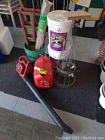 Lot overview showing Toro blower vac, garden stakes, tomato cages, pails of ice melt, plastic buckets and fuel can on garage floor.