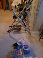 Side view of the Gazelle Freestyle Crosstrainer showing frame, foot pedals, and resistance tubes, with workout tapes and manuals placed on the floor nearby.