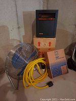 Photo showing all items in the lot including fan, heater on box, yellow extension cord, and boxed Square D panel