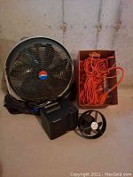 Photo showing large industrial fan, compact heater, small battery-operated fan, and orange extension cords.
