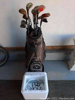 Full view of golf clubs in Callaway bag with styrofoam cooler of golf balls in front.