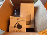 Box containing Google Home smart speaker device and Google Chromecast Ultra streaming device in unopened packaging.