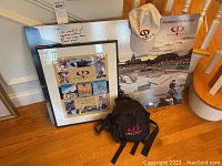Photo showing three framed Gravity Games prints, white baseball cap, and black shoulder bag all placed near a staircase.
