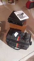 Kodak Supermatic 20 sound projector sitting on box with instruction manual on top and black nylon camera bag featuring red and yellow stripes in front.