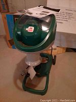 Green Mosquito Magnet Liberty Plus device with top opening and attached owner's manual on top.