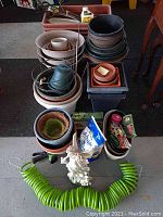 Full view of stacked plastic and ceramic planters, assorted fertilizer packets, garden nymph statue, and coiled green garden hose.