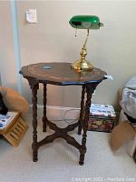 Wood octagonal side table with carved edge and turned spindle legs shown with lamp on top.