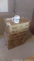 Stacked boxes labeled as stoneware mugs and a single mug on top showing the logo.