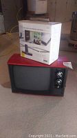 Red MGA TV alongside boxed Terk TV5 antenna on concrete floor in basement setting.