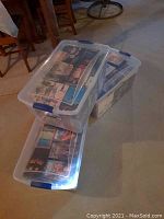 Three clear plastic storage totes stacked containing various VHS movie tapes visible through the lids.