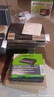 Three electronic devices arranged: Sylvania VHS deck on top of box, Insignia converter box in original packaging in front. Some papers and cables nearby.