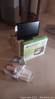 Sansui 22in LED TV on cardboard box with original box beneath and Wii console accessories in plastic bags on floor in basement setting