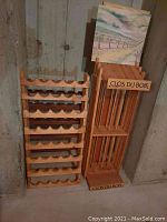 Two wooden wine racks side-by-side against a concrete wall. The upright rack displays 'Clos Du Bois' branding.