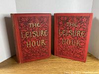 Front view of two red hardcover books titled 'The Leisure Hour' with floral designs and gold lettering.