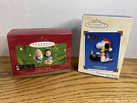 Two Hallmark Keepsake ornament boxes displayed side by side on a flat surface, showing the packaging and artwork of Snoopy and Charlie Brown Peanuts ornaments.