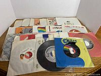 A spread of 27 various 7-inch 45 RPM vinyl records from the 1970s and 1980s, featuring pop music singles in assorted paper sleeves.