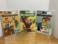 Three graded Woody Woodpecker comics #16, #17, #18 displayed upright, showing front covers and protective sleeves.