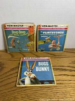 Photo showing three View-Master reel packets: Beep Beep The Road Runner, The Flintstones, and Bugs Bunny, each with cartoon-themed cover art and indicating 21 stereo pictures per packet.