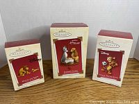 Photo showing all three original Hallmark Keepsake Disney-themed Christmas ornaments in their boxes arranged on a wooden surface.