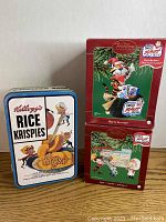 Three Kellogg's Christmas ornaments in boxes, with a Rice Krispies tin box for reference.